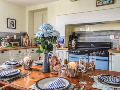 A kitchen with a wooden dining table set for four with plates napkins glasses a bottle flowers and candles at Towyn Lodge in Trearddur Bay