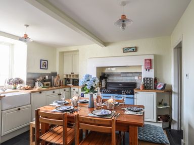 A kitchen with wooden dining table set for four and a blue stove at Towyn Lodge in Trearddur Bay