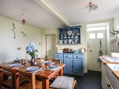 A kitchen dining area with a wooden table set for four and a blue cabinet with mugs and a kettle at Towyn Lodge in Trearddur Bay