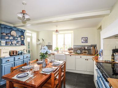 A kitchen with a wooden dining table set for four and blue and white cabinetry at Towyn Lodge in Trearddur Bay