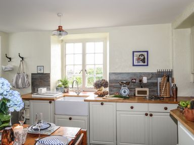 A kitchen with a wooden countertop a white farmhouse sink and a window above it at Towyn Lodge in Trearddur Bay