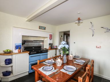 A kitchen dining area with a wooden table set for four and a blue stove at Towyn Lodge in Trearddur Bay