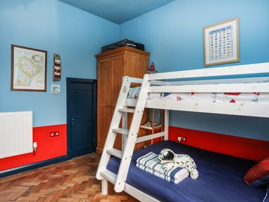A bedroom with bunk beds a wooden wardrobe framed pictures on blue and red walls at Towyn Lodge in Trearddur Bay