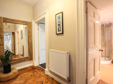 A hallway with a large wooden framed mirror a white door open to a bathroom with a shower Towyn Lodge Trearddur Bay