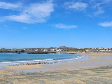 A sandy beach with small waves and houses in the background at Towyn Lodge in Trearddur Bay