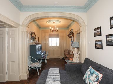A living room with a gray sofa and a piano near the door at Towyn Lodge in Trearddur Bay