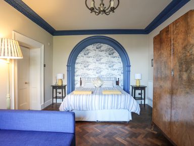 A bedroom with a double bed under a blue arch with sailboat wallpaper at Towyn Lodge in Trearddur Bay