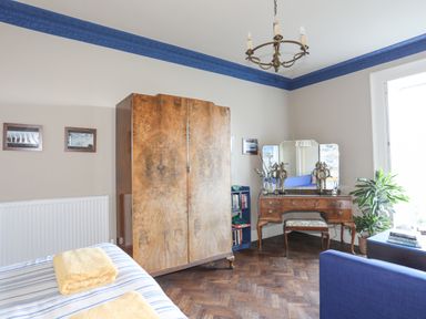 A bedroom with a wooden wardrobe a dressing table a bookshelf and a blue chair at Towyn Lodge in Trearddur Bay