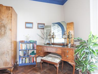 A room with a wooden dresser and mirror a bookcase with books and two framed pictures on the wall at Towyn Lodge in Trearddur Bay
