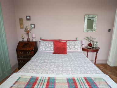 A bedroom with a bed covered in a floral duvet and a red pillow with bedside tables and wall decorations at Towyn Lodge in Trearddur Bay