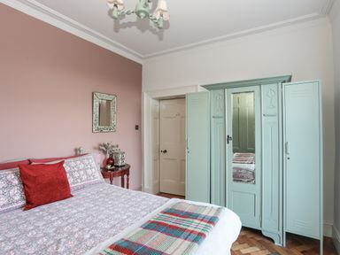 A bedroom with a bed with patterned bedding a red pillow a side table with a plant and decorative items a mirror on the wall and a wardrobe with mirrored doors at Towyn Lodge in Trearddur Bay