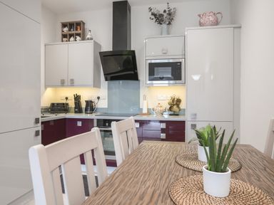 A kitchen with white and maroon cabinets a wooden table with plants on placemats and kitchen appliances at The Pot Loft in Benllech