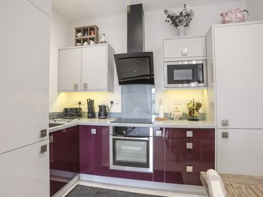 A kitchen with purple lower cabinets gray upper cabinets a built in oven microwave and black extractor hood at The Pot Loft in Benllech