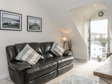 A small living area with a black leather sofa and cushions a lamp on a side table pictures on the wall and a door leading to a balcony at The Pot Loft in Benllech
