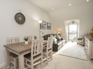 A dining table with chairs a sofa armchair and sideboard in a living room with a balcony door at The Pot Loft in Benllech
