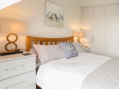 A bedroom with a wooden bed frame white bedding bedside tables with lamps and a wardrobe at The Pot Loft in Benllech