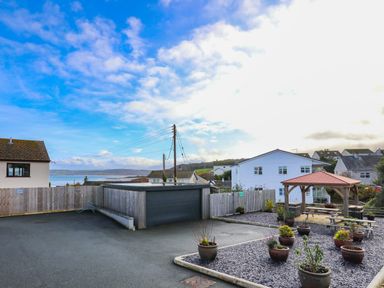 An outdoor area with potted plants gravel, a wooden gazebo with picnic tables, a fenced garage, and houses in the background at The Pot Loft in Benllech