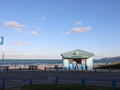 An ice cream kiosk by a beach with benches and a flagpole at The Pot Loft in Benllech