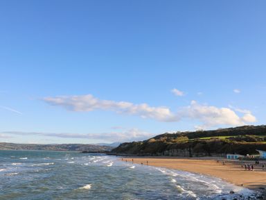 A beach with waves and people walking near cliffs and hills at The Pot Loft in Benllech