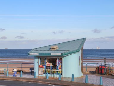 A small ice cream kiosk by a beach with the sea and ships in the background at The Pot Loft in Benllech
