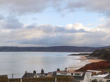 A coastal view with rooftops in the foreground a sandy beach and hills across the water at The Pot Loft in Benllech