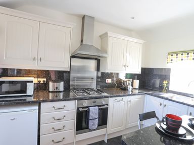 A kitchen with white cabinets a microwave toaster gas stove oven and a sink with a window at Tyn Towyn - Bwthyn Carreg in Trearddur Bay