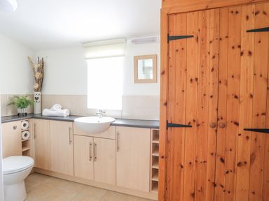 A bathroom with a toilet a sink a wooden cabinet and a window with a roller blind at Tyn Towyn - Bwthyn Carreg in Trearddur Bay