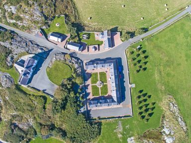 An aerial view of a large building complex with an inner courtyard and surrounding roads and fields at Tyn Towyn - Bwthyn Carreg in Trearddur Bay