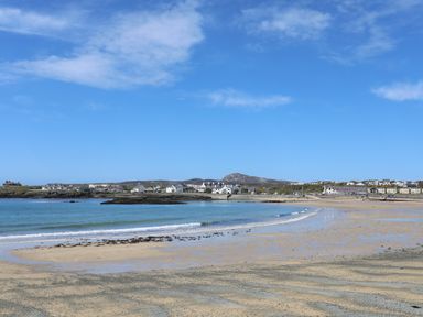 A sandy beach with small waves and houses in the distance at Tyn Towyn - Bwthyn Carreg in Trearddur Bay