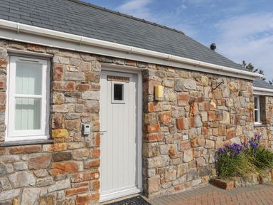 Exterior stone wall of a building with a white door and two white windows at Tyn Towyn - Bwthyn Carreg in Trearddur Bay