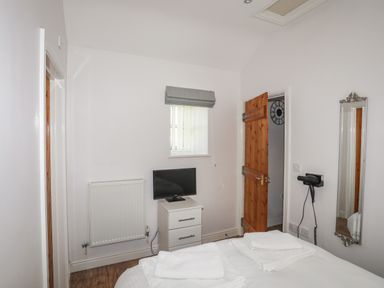 A bedroom with a bed, folded towels, a small cabinet with a television, a wall-mounted hairdryer, a mirror, and a wooden door at Tyn Towyn - Bwthyn Carreg in Trearddur Bay