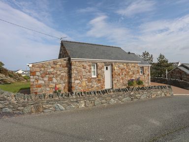 A stone cottage with a slate roof and small flower beds outside at Tyn Towyn - Bwthyn Carreg in Trearddur Bay