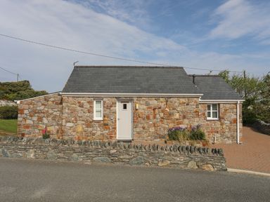 A stone cottage with a grey slate roof and a white door at Tyn Towyn - Bwthyn Carreg in Trearddur Bay