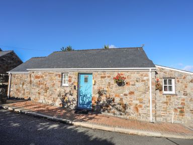 A stone cottage with a blue door and windows with hanging flower baskets at Tyn Towyn - Bwthyn Haf in Trearddur Bay
