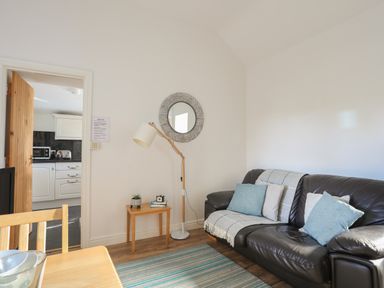 A living room with a black leather sofa cushions and a lamp next to a wooden table at Tyn Towyn - Bwthyn Haf in Trearddur Bay