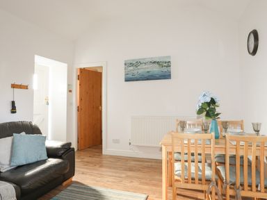 A living room with a black leather sofa and wooden dining table with chairs at Tyn Towyn - Bwthyn Haf in Trearddur Bay