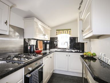 A kitchen with white cabinets a gas stove sink and a fruit bowl at Tyn Towyn - Bwthyn Haf in Trearddur Bay