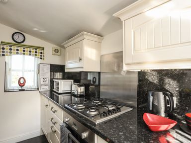 A kitchen countertop with a gas stove microwave toaster electric kettle and red bowl at Tyn Towyn - Bwthyn Haf in Trearddur Bay