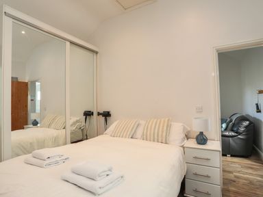 A bedroom with a double bed, bedside table with lamp, striped pillows, and mirrored wardrobe doors at Tyn Towyn - Bwthyn Haf in Trearddur Bay