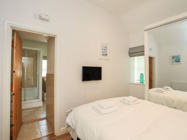 A bedroom with a bed and folded towels a wall-mounted tv and a door leading to a bathroom at Tyn Towyn - Bwthyn Haf in Trearddur Bay