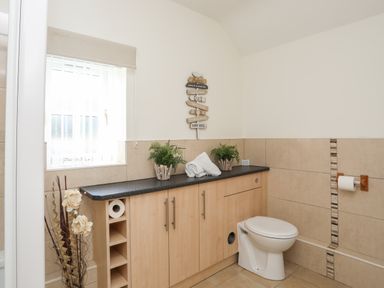 A bathroom with a toilet wooden cabinets and a window with blinds at Tyn Towyn - Bwthyn Haf in Trearddur Bay