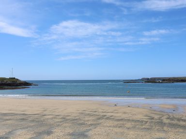 A sandy beach with calm sea and rocky shorelines at Tyn Towyn - Bwthyn Haf in Trearddur Bay