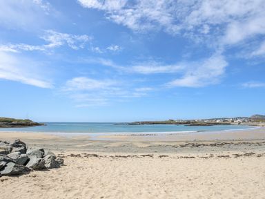 A sandy beach with rocks and calm sea under a blue sky at Tyn Towyn - Ty Glas in Trearddur Bay