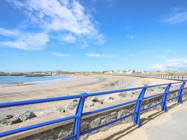A beach with sand and sea separated by a blue railing and a stone wall at Tyn Towyn - Ty Glas in Trearddur Bay