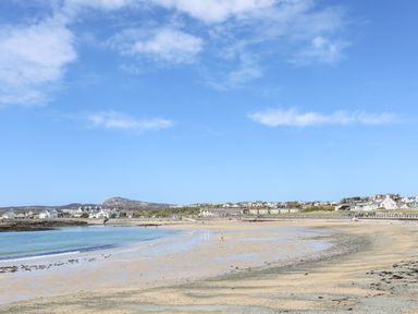 A sandy beach with calm water and houses in the background at Tyn Towyn - Ty Glas in Trearddur Bay