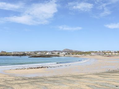 A sandy beach with shallow water and waves near a coastal village with houses and hills in the background at Tyn Towyn - Ty Glas in Trearddur Bay