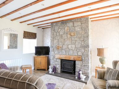 A living room with a stone fireplace wooden beams on ceiling and a television on a wooden cabinet at Tyn Towyn - Ty Glas in Trearddur Bay