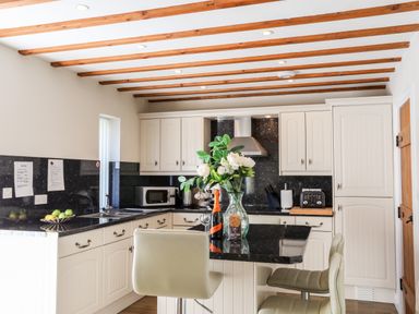 A kitchen with white cabinets black countertops a microwave toaster and flowers on a kitchen island at Tyn Towyn - Ty Glas in Trearddur Bay