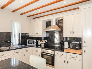 A kitchen with white cabinets black countertops a microwave kettle toaster and oven at Tyn Towyn - Ty Glas in Trearddur Bay