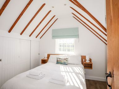 A bedroom with a bed pillows and folded towels under a window with a green shade and wooden beams on the ceiling at Tyn Towyn - Ty Glas in Trearddur Bay